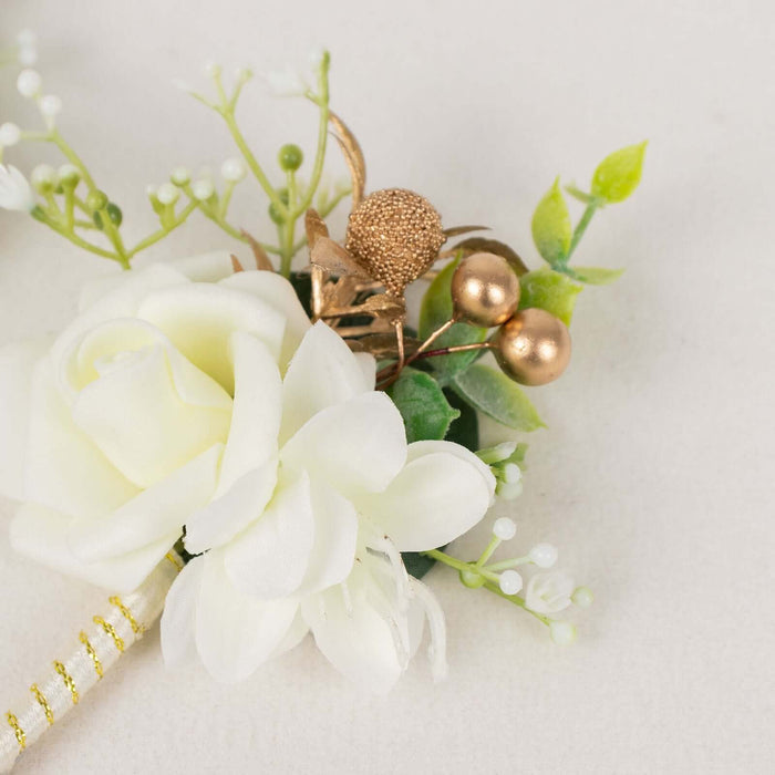 White flower boutonnière with gold accents and greenery on a light background.