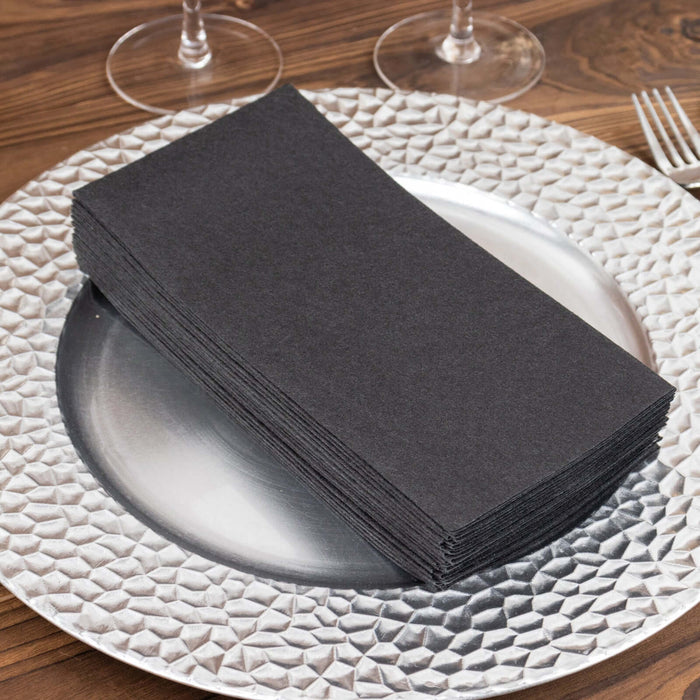 Black napkins stacked on a textured silver charger plate.