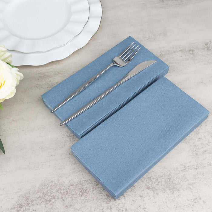 Blue linen napkin set with silver fork and knife on a textured surface.