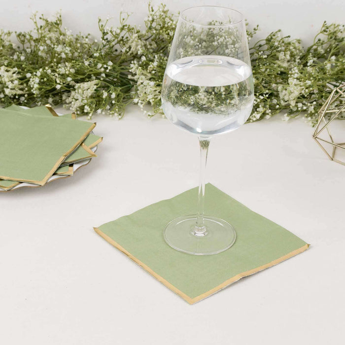 Green paper napkin with gold edges under a glass of water on a table.