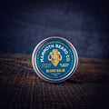 Closed tin of Cedar & Mint Beard Balm by Mammoth Beard Co on dark wood surface, natural beard conditioner with woods, mint and vanilla scent.