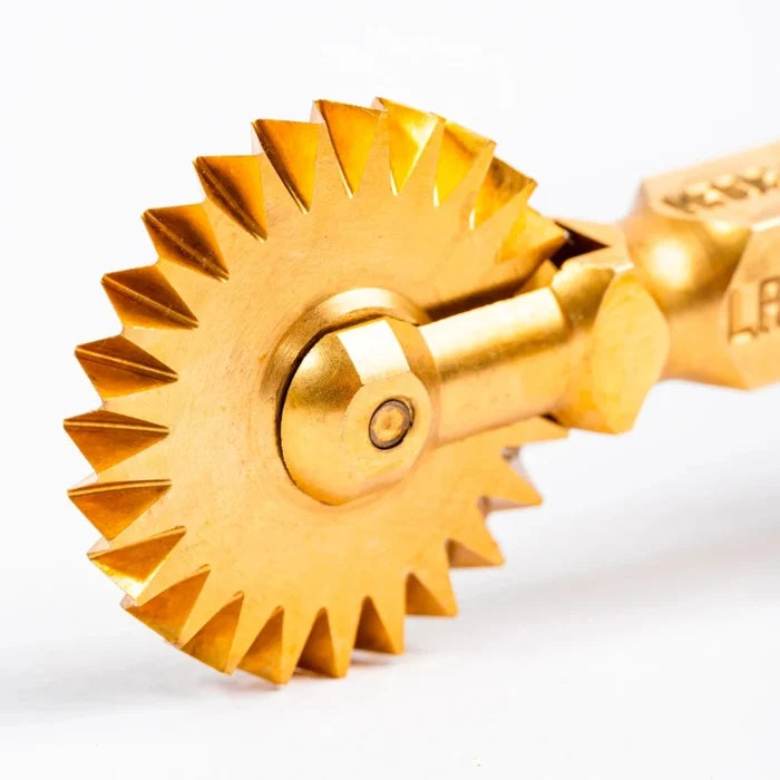 Gold-colored Pasta cutter with a gear-like design on a white background.