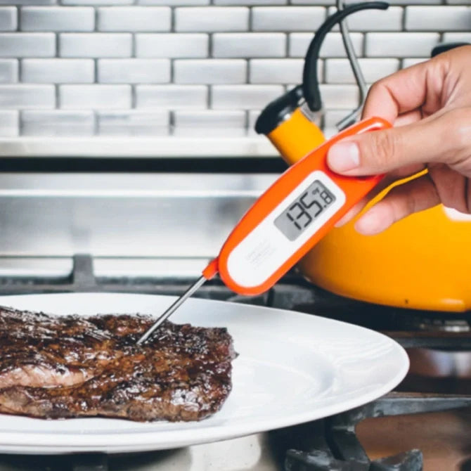 Digital thermometer inserted into a steak on a plate with a kitchen background