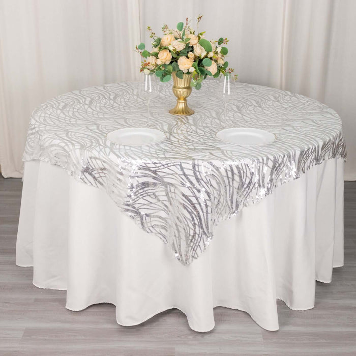 Round table with elegant silver-patterned tablecloth and floral centerpiece.