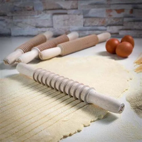 A beige wooden pasta cutter with a rolling pin shape, designed for cutting Pappardelle pasta.