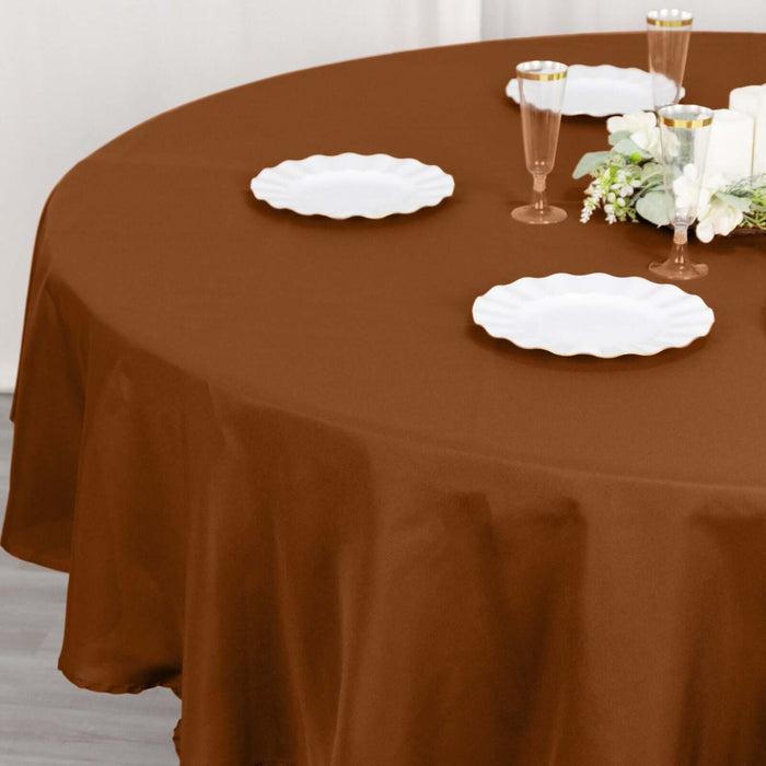 Brown round tablecloth draped over a table set with white plates and glasses.