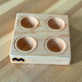 A square maple wood ravioli mold with 4 circular indentations, placed on a wooden surface.