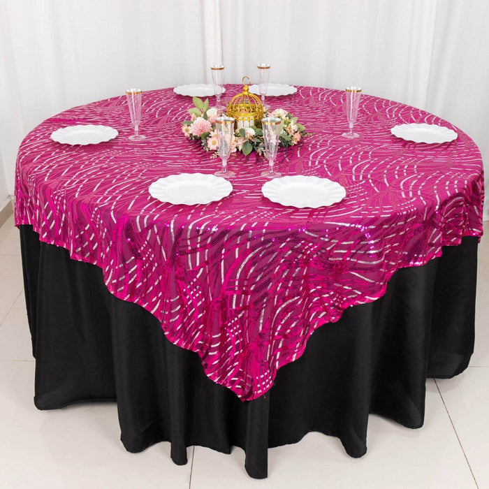 Round pink patterned tablecloth draped over a black table with plates and floral centerpiece.