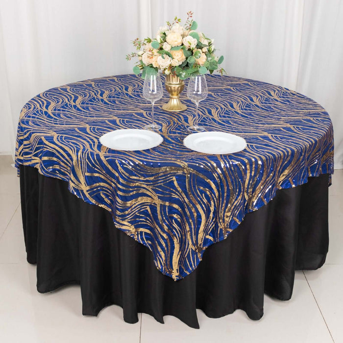 Round table covered with a blue and gold patterned tablecloth, decorated with flowers and plates.