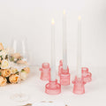Pink candle holders with white candles and a wine glass beside roses.