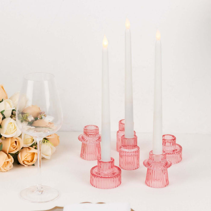 Pink candle holders with white candles and a wine glass beside roses.