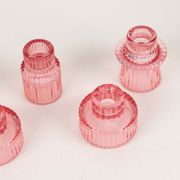 Pink glass candle holders in various sizes against a plain backdrop