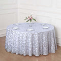Round lace tablecloth in light gray on a wooden table with plates and flowers.