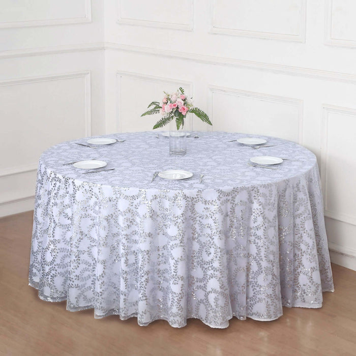 Round lace tablecloth in light gray on a wooden table with plates and flowers.